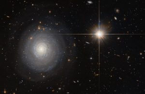 This image was taken by the NASA/ESA Hubble Space Telescope’s Advanced Camera for Surveys (ACS), and shows a starburst galaxy named MCG+07-33-027. This galaxy lies some 300 million light-years away from us, and is currently experiencing an extraordinarily high rate of star formation — a starburst. Normal galaxies produce only a couple of new stars per year, but starburst galaxies can produce a hundred times more than that! As MCG+07-33-027 is seen face-on, the galaxy’s spiral arms and the bright star-forming regions within them are clearly visible and easy for astronomers to study. In order to form newborn stars, the parent galaxy has to hold a large reservoir of gas, which is slowly depleted to spawn stars over time. For galaxies in a state of starburst, this intense period of star formation has to be triggered somehow — often this happens due to a collision with another galaxy. MCG+07-33-027, however, is special; while many galaxies are located within a large cluster of galaxies, MCG+07-33-027 is a field galaxy, which means it is rather isolated. Thus, the triggering of the starburst was most likely not due to a collision with a neighbouring or passing galaxy and astronomers are still speculating about the cause.