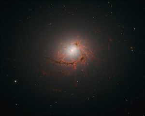 This picture, taken by Hubble’s Wide Field Camera 3 (WFC3), shows NGC 4696, the largest galaxy in the Centaurus Cluster. The new images taken with Hubble show the dusty filaments surrounding the centre of this huge galaxy in greater detail than ever before. These filaments loop and curl inwards in an intriguing spiral shape, swirling around the supermassive black hole at such a distance that they are dragged into and eventually consumed by the black hole itself.
